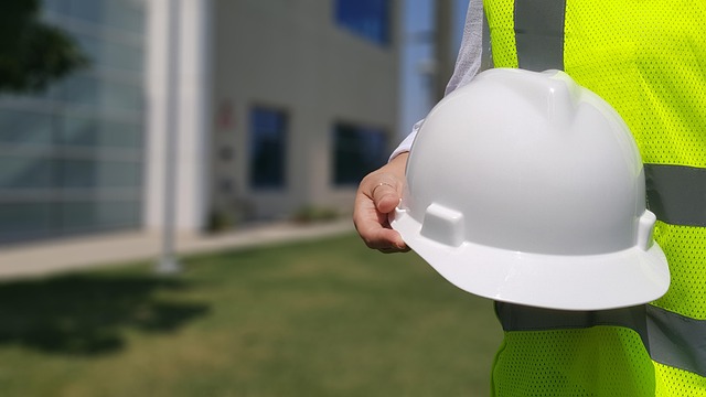 HVAC Technician - Man with safety vest and white hard hat standing on a lawn in front of a tall building
